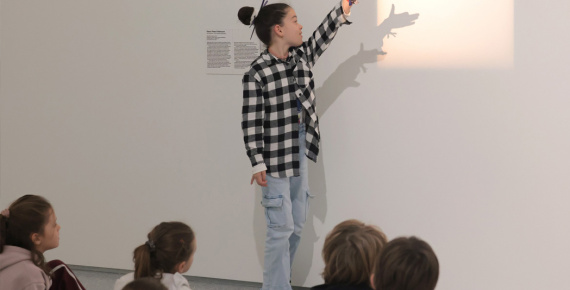 Enfant jouant avec la lumière d'une œuvre d'art, se tenant devant un groupe d'enfants assis. 